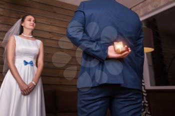Groom in suit holding wedding rings and making a proposal of marriage to the bride in white dress and veil