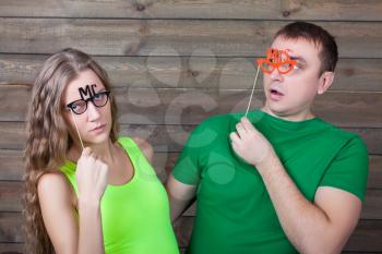 Playful couple with funny glasses on a sticks, wooden background. Fun photo props and accessories for shoots