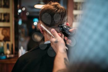 Barber hands makes hairstyle of the client man by clipper. Male person sitting at the mirror in barbershop
