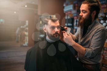 Haircutter makes hairstyle of the client man in black salon cape by clipper. Barbershop concept