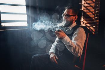 Portrait of bearded man in glasses sitting on a chair and smoking pipe. Writer, journalist, literature author, blogger or poet concept