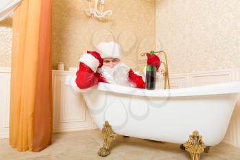 Funny drunk Santa Claus with alcohol bottle in hand sleeping in a bath. Christmas humor