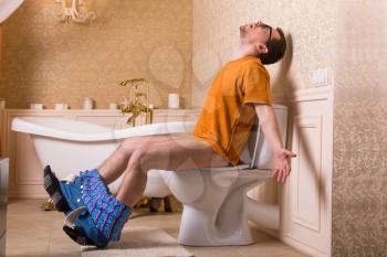 Man with pants down sitting on the toilet bowl. Bathroom interior in retro style on background
