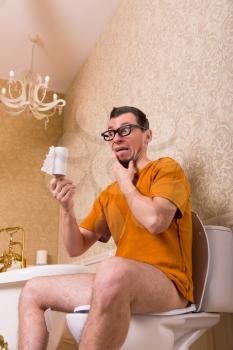 Surprised man in glasses sitting on the toilet bowl, out of paper