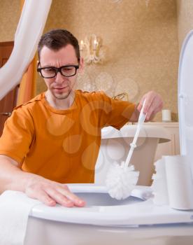 Man in glasses cleans the toilet bowl by brush. Luxury bathroom interior on background