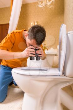 Curious man with binoculars looking in the toilet. Luxury bathroom interior on background