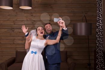Smiling bride and groom making selfie on mobile phone, wooden background.