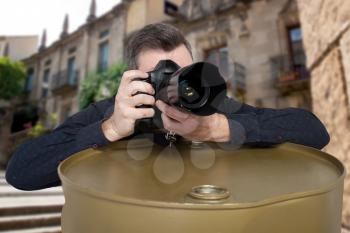 Photographer takes a picture on digital camera leaning on an iron barrel, old building on background