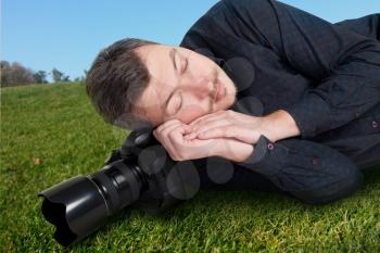 Male photographer with digital camera sleeping on a meadow