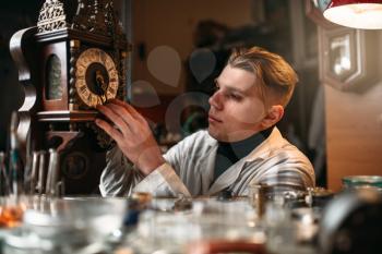 Watchmaker adjusts the mechanism of old wall clock in the workshop.