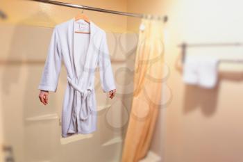 Invisible woman in white bathrobe hanging on a hanger in bathroom. Invisibility fantasy concept, transparent female person