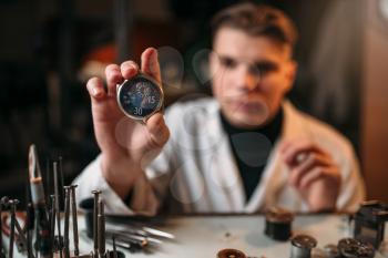 Watch maker holding wrist watch in hand. Watchmaking tools on the table