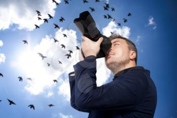 Portrait of male photographer with camera taking a picture, flock of birds flying in the sky on background