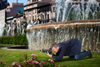Photographer taking macro picture of flowers on digital camera, fountains and old building with columns on background