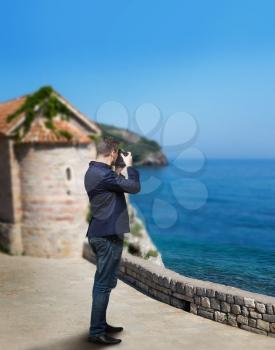 Male photographer taking picture of sea coast on digital camera