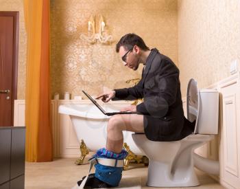 Man in glasses with laptop sitting on the toilet bowl. Luxury bathroom interior in vintage style on background