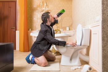 Funny man drink alcohol sitting against the toilet bowl. Luxury bathroom interior on background