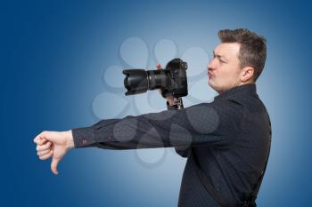 Photographer with professional digital camera shows thumb down, blue background