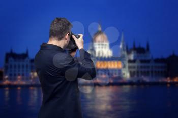 Professional photographer with  digital photo camera takes night pictures of palace on the river