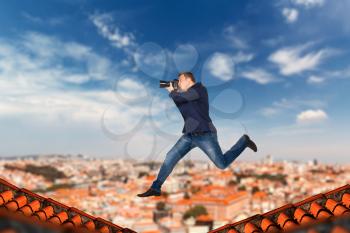 Professional male photographer with digital camera takes pictures jumping on the roofs of houses