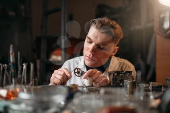 Watchmaker holding with tweezers a gear of old hours. Broken mechanical watches repairing