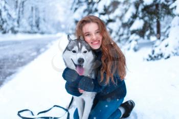 Woman hugs with siberian husky, friendship forever, snowy forest on background. Cute girl walk in park with charming dog