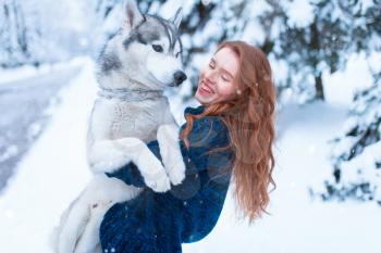 Woman playing with siberian husky, friendship forever, snowy forest on background. Cute girl walk in park with playful pet