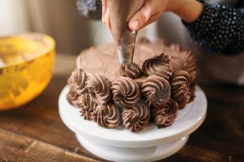Woman cook decorate chocolate cake with culinary syringe. Kitchen on background. Homemade dessert decoration