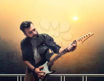 Male brutal solo guitarist with electric guitar against cityscape