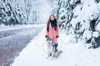 Siberian husky sitting near young woman, snowy forest on background. Cute girl with charming dog