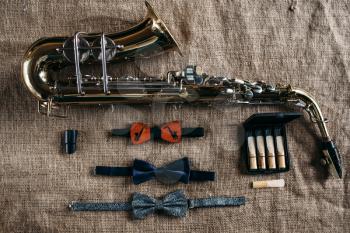 Saxophone, mouthpieces and bowtie on grunge sack background, closeup view. Brass band instrument concept. Classical sax, jazz music