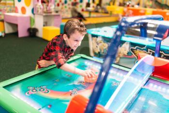 Active boy plays air hockey in entertainment center. Happy childhood. Sport game attraction