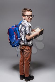 Little child with school bag and book, studio photo shoot. Young pupil with backpack and textbook. Boy with schoolbag