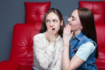 Two pretty girls gossiping on red leather couch. Women secrets