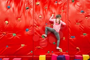 Girl climbing on a wall in childrens attraction playground. Entertainment center. Happy childhood