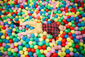 Little boy lying in a pile of colorful inflatable balloons in childrens entertainment center. Happy childhood