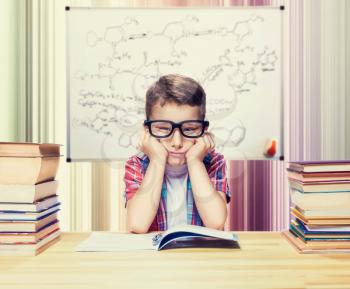 Little boy learns homework in the school library. Pupil in glasses against book shelves