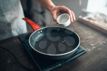 Male person hands pour oil in a frying pan. Food cooking