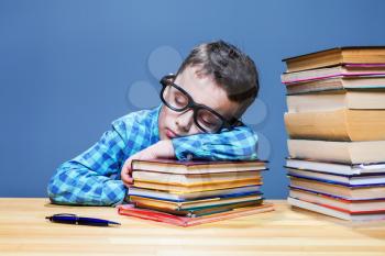 Cute child asleep at the desk in school library. Pupil in glasses against many books