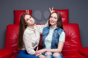Female friendship, leisure of happy girls. Two pretty women sitting on red leather couch