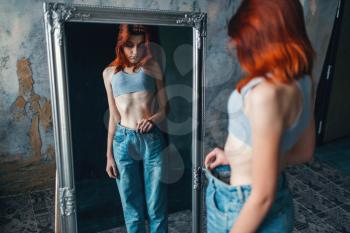 Thin woman tries on big size jeans against mirror, weight loss, anorexia. Fat or calories burning concept, medical illness