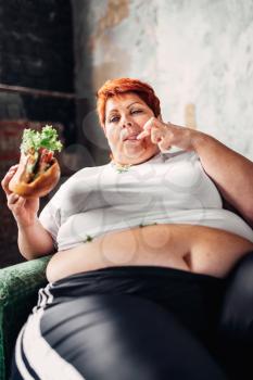 Fat woman sits in a chair and eats sandwich, overweight, fatty and bulimic. Unhealthy lifestyle, obesity