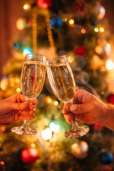 Two hands clink glasses with champagne, christmas tradition, romantic celebration. Xmas symbol to drink sparkling wine