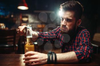 Sad man sitting at the bar counter and opens the bottle with alcohol beverage. Male person in pub, alcoholism