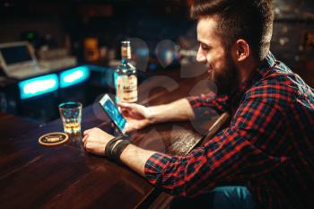 Male person with mobile phone sitting at the bar counter, relaxation with alcohol. Happy guy having fun, leisure in pub