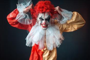 Scary bloody clown tears his hair, jerk in anger. Man with makeup in carnival costume, crazy maniac