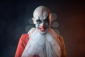 Portrait of crazy bloody clown, face in blood. Man with makeup in halloween costume