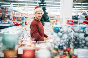 Young man chooses christmas decorations in supermarket, holiday purchasing is a tradition. December shopping