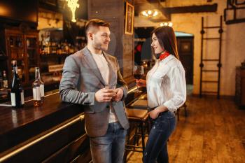 Man and woman drinks red wine at wooden bar counter. Couple leisures in pub, husband and wife relaxing together in a nightclub
