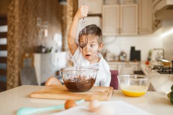 Young kid mixing melted chocolate in a bowl. Cute boy cooking on the kitchen. Happy child prepares sweet dessert at the counter